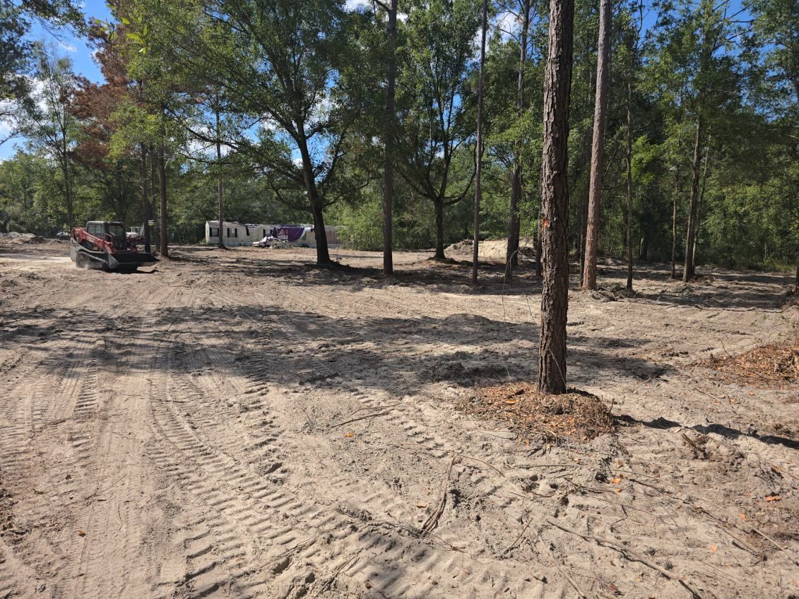 A sandy clearing with a small excavator, trees in the background. Construction site.