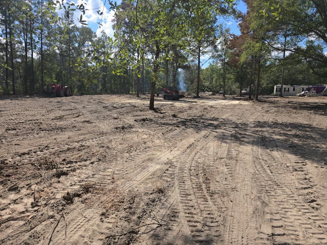 Cleared sandy area with tire tracks, trees in the background, and construction in the distance.