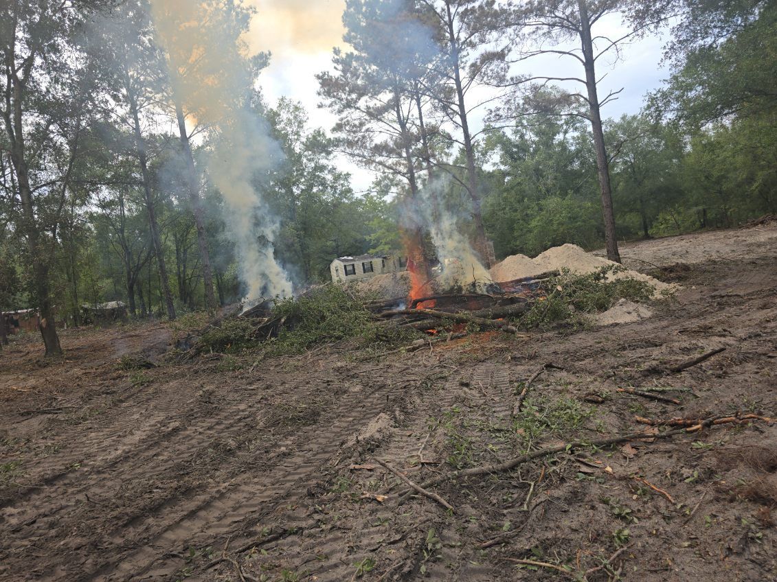 Smoke rising from a brush fire in a deforested area of a forest; trees in the background.