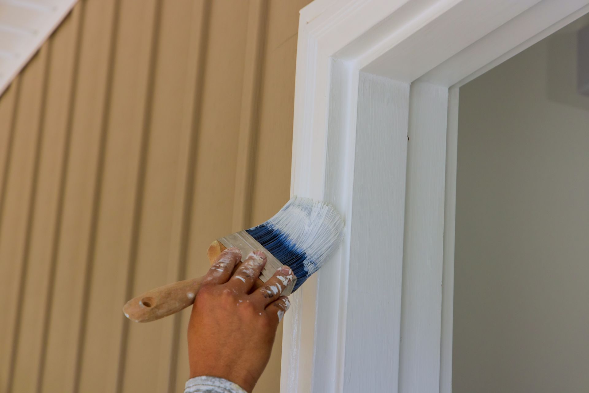 Person painting white trim around a door with a paintbrush.