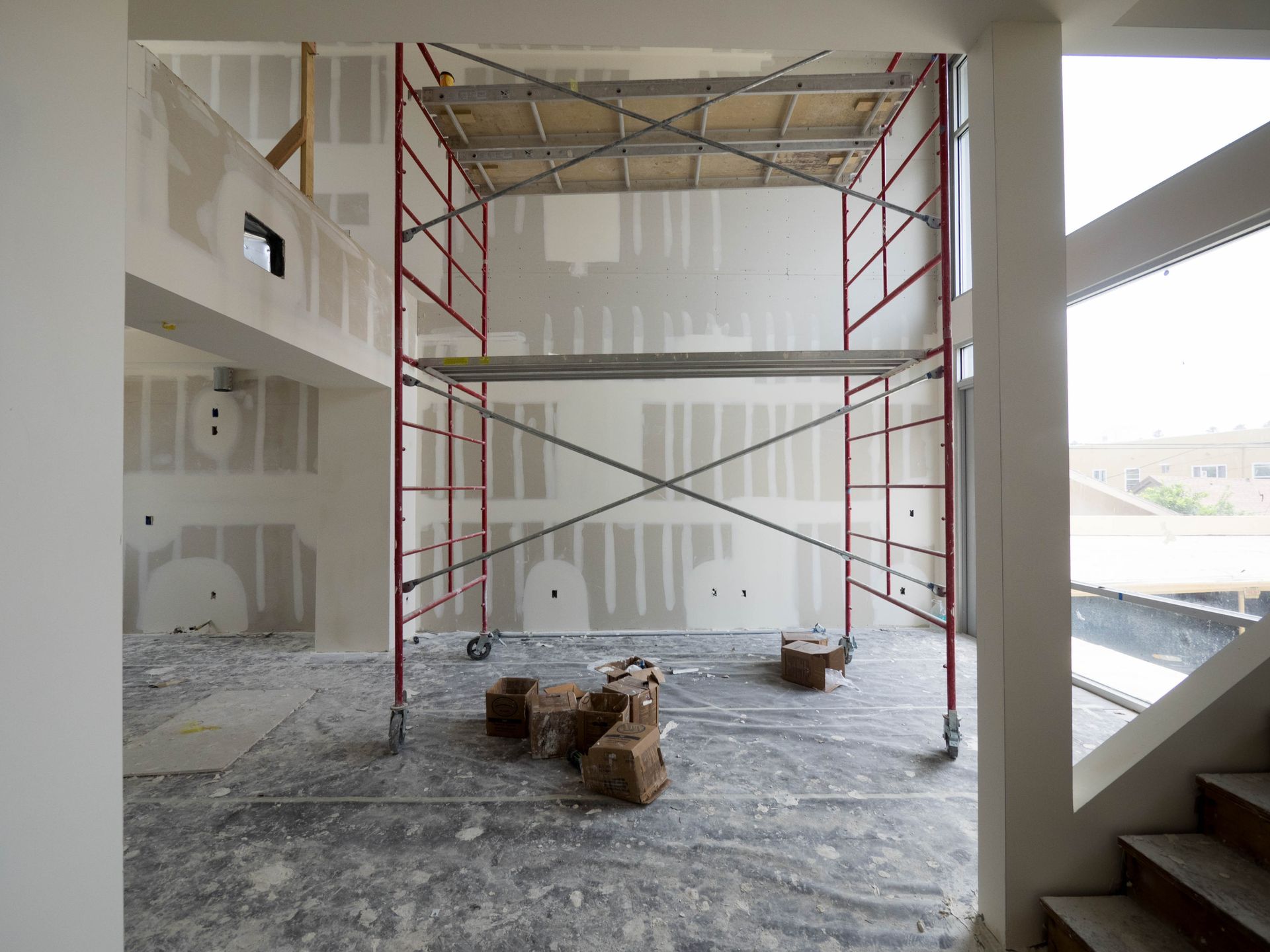 Interior construction site with red scaffolding; drywall on walls and floor debris.