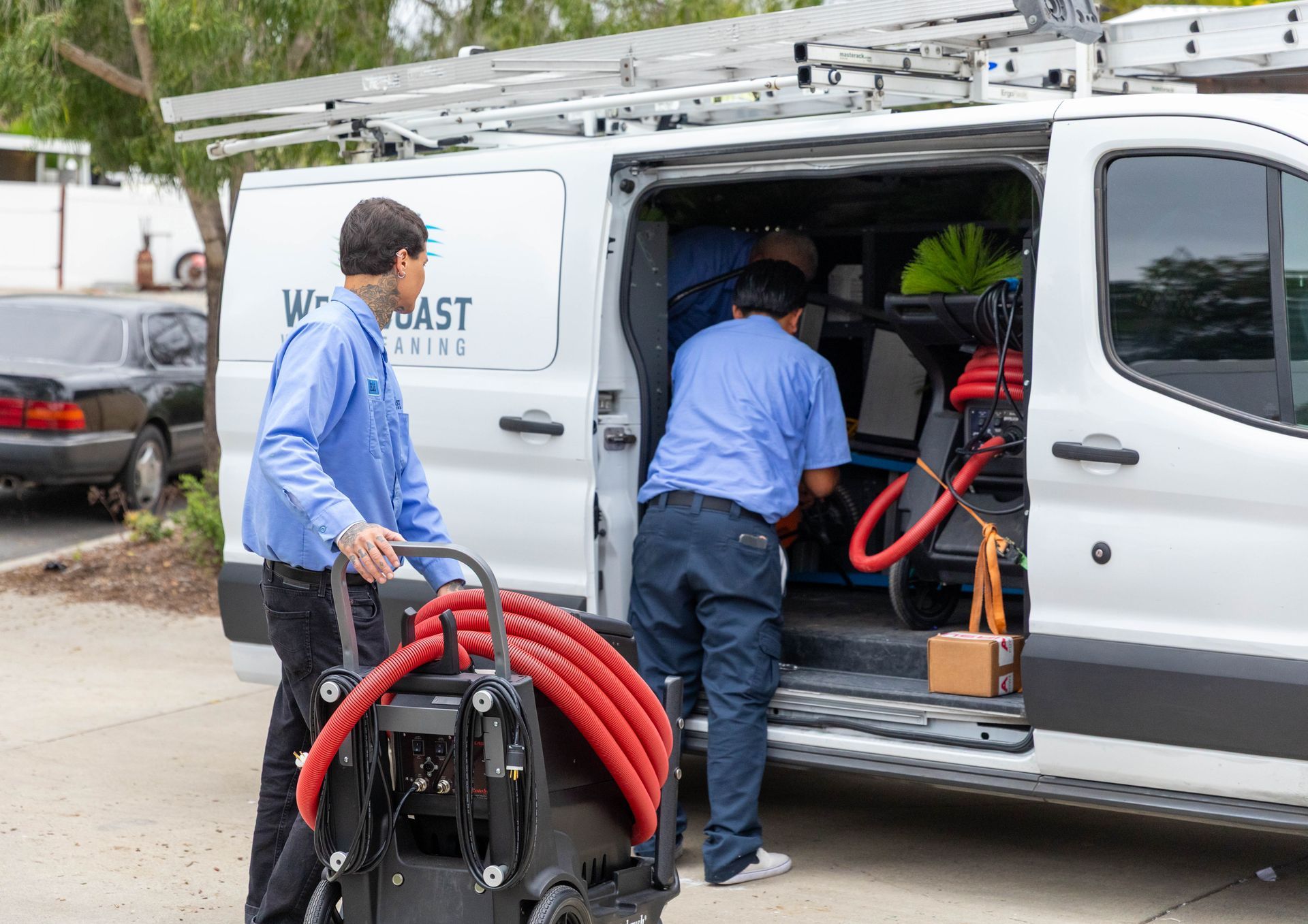 Two workers in blue shirts load professional cleaning equipment into the back of a white service van.