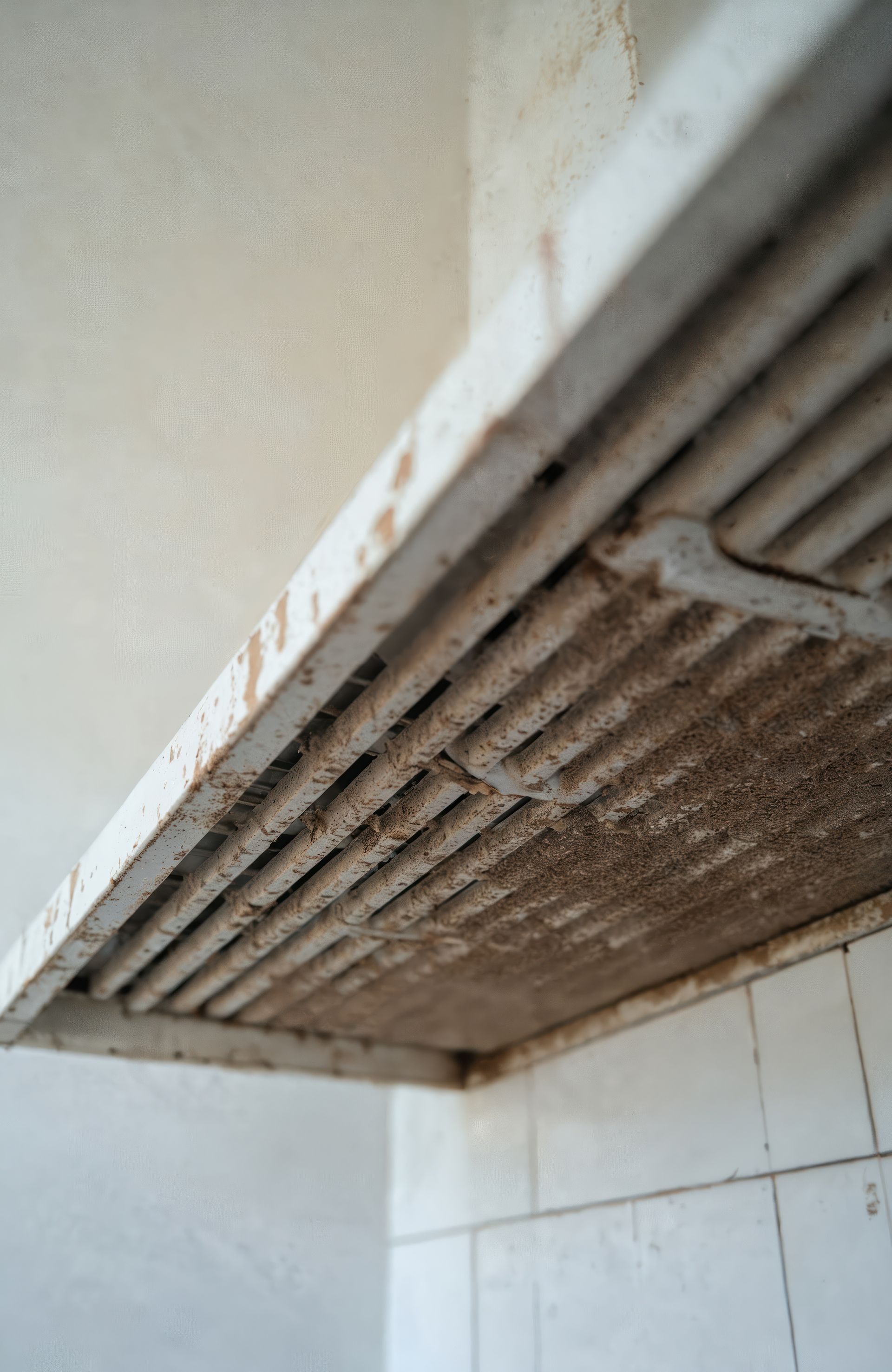A technician uses a handheld device attached to a blue portable unit to clean a ceiling vent in a hallway.