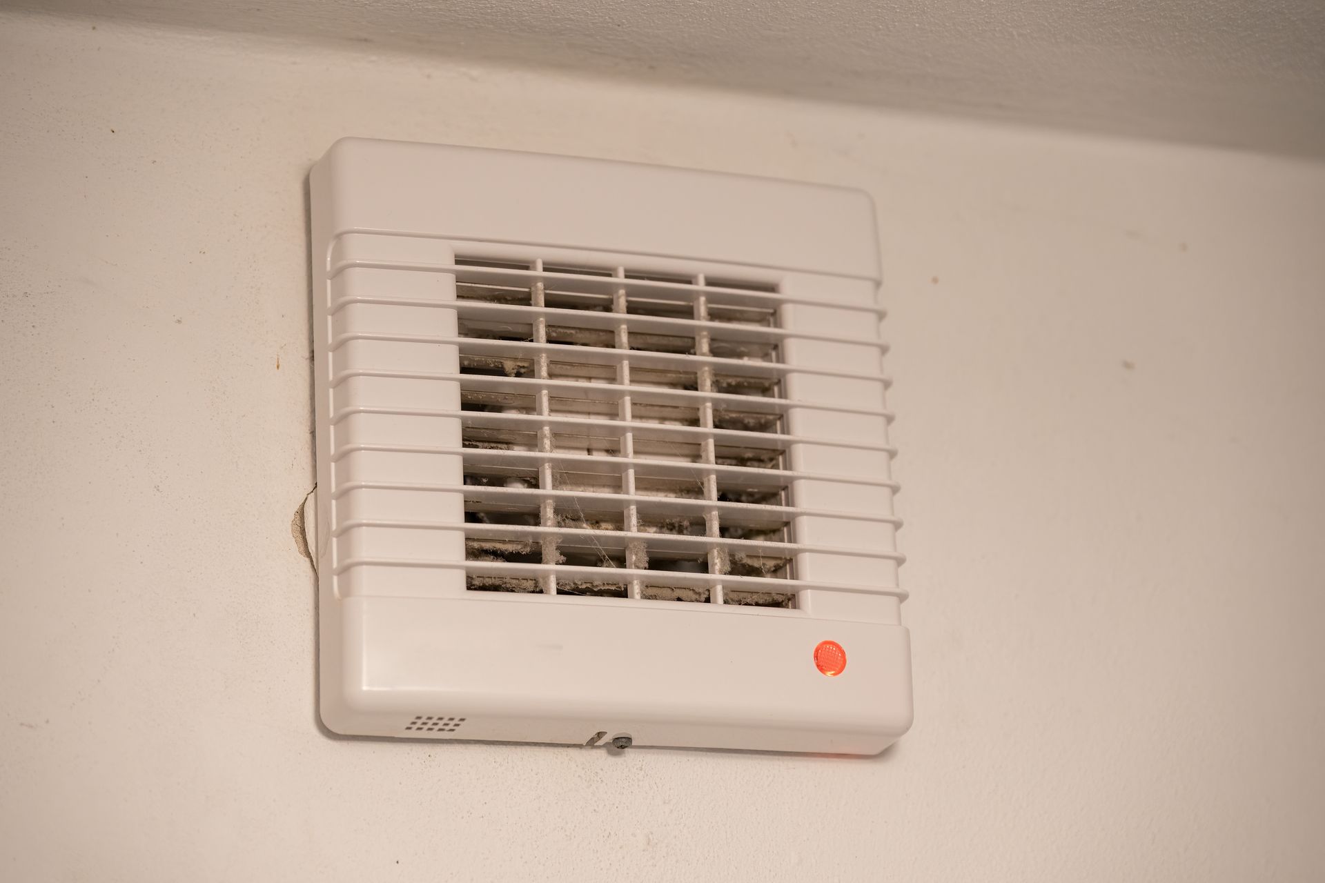 A technician uses a handheld device attached to a blue portable unit to clean a ceiling vent in a hallway.