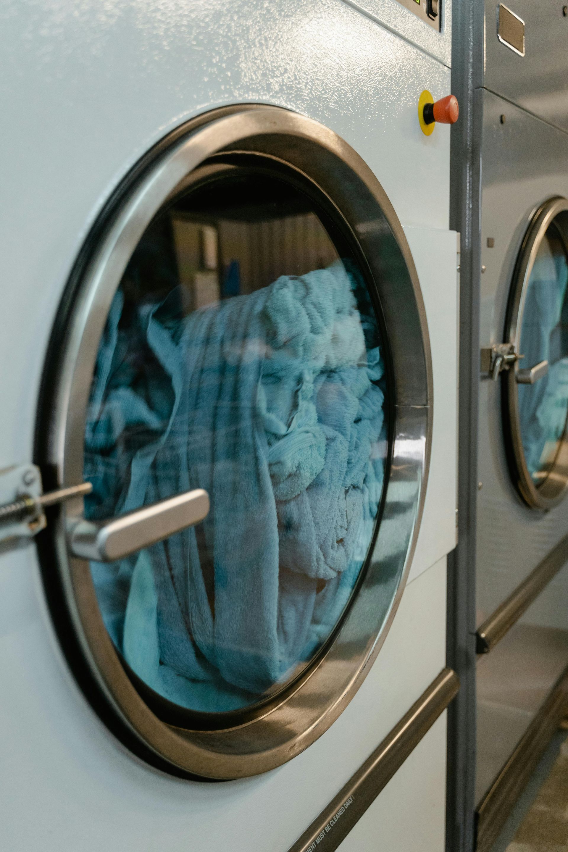 Blue towels tumbling in industrial front-loading dryers in a laundry room