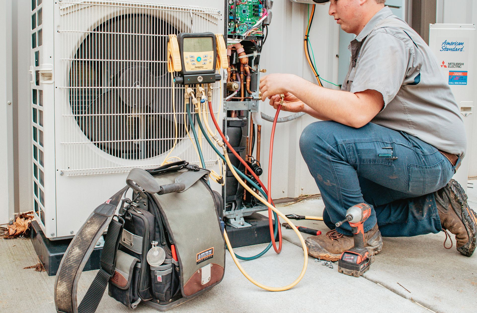 HVAC technician kneeling, working on outdoor air conditioning unit, using tools.