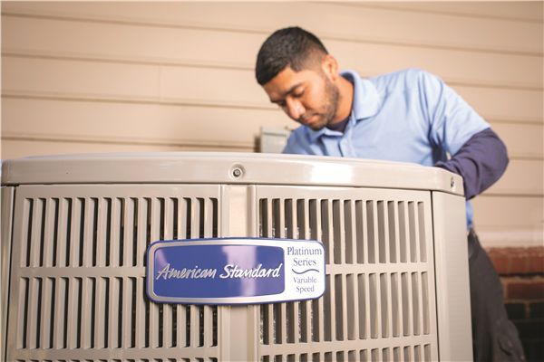 HVAC technician inspecting an American Standard air conditioning unit outside a building.