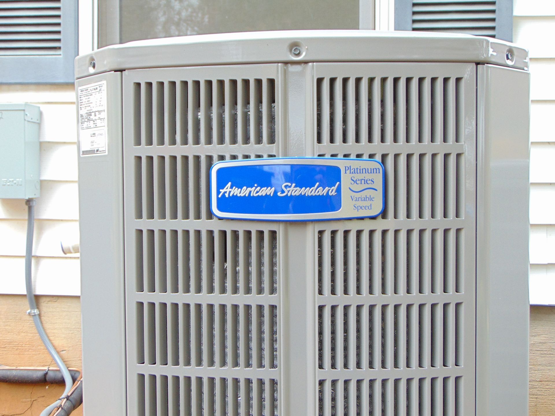 American Standard air conditioning unit outdoors with gray metal grill.