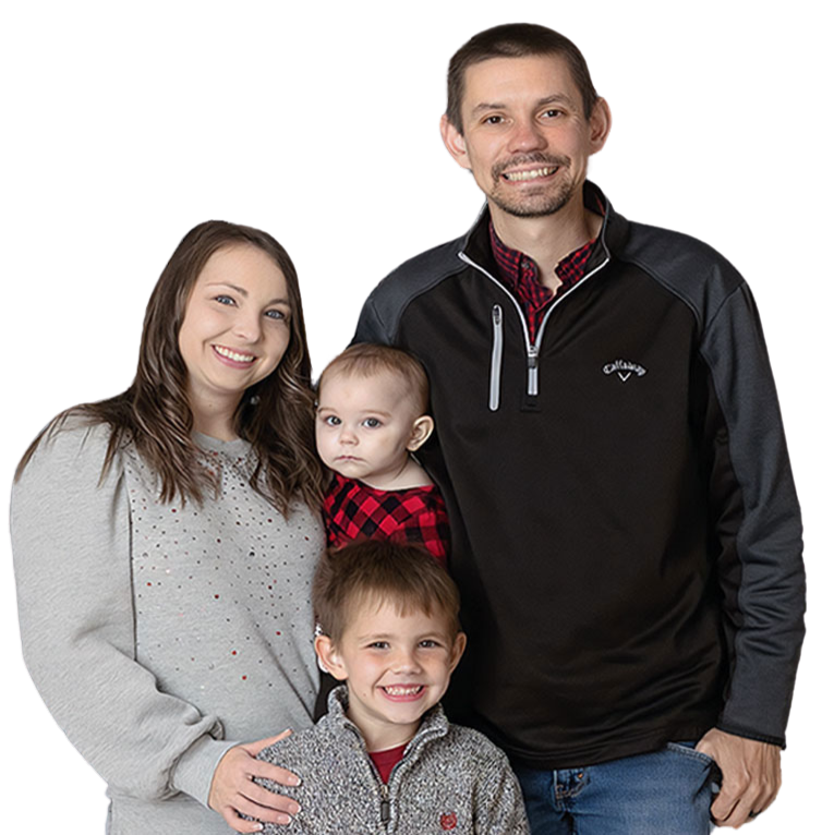 Family of four smiling, posing for a photo. Woman in gray sweater, man in black jacket, two children.