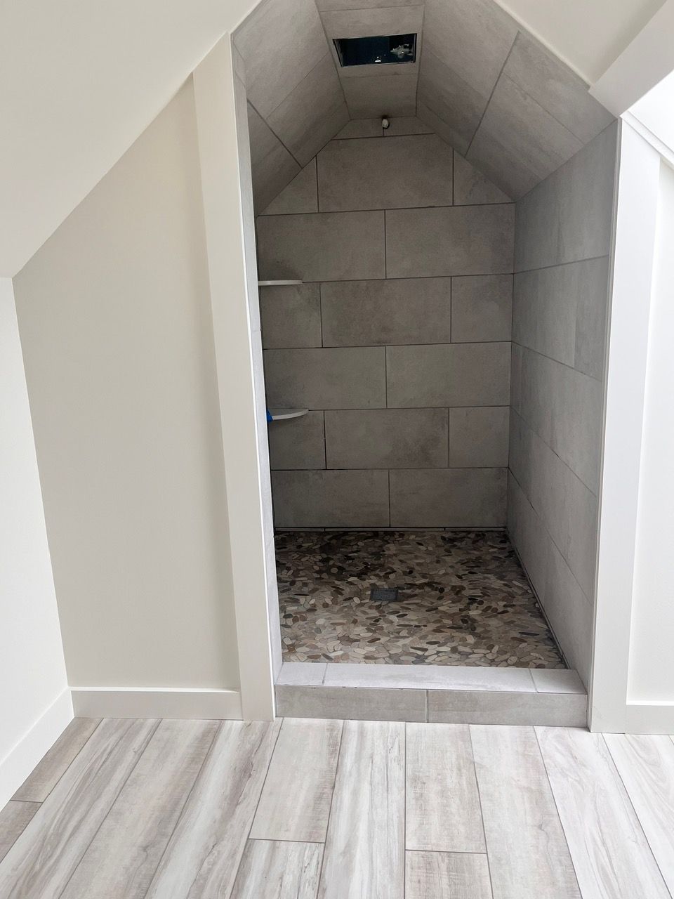 A bathroom with a walk in shower under a staircase.