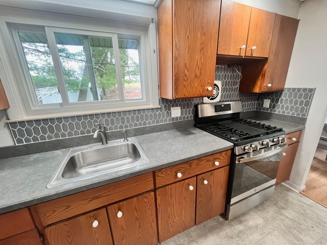 A kitchen with wooden cabinets , a stove , a sink , and a window.
