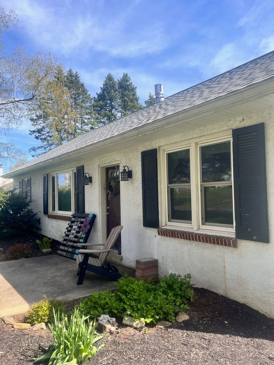 A white house with black shutters and a chair on the porch.