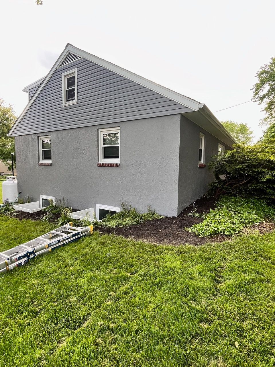 A house with a ladder in the grass in front of it.