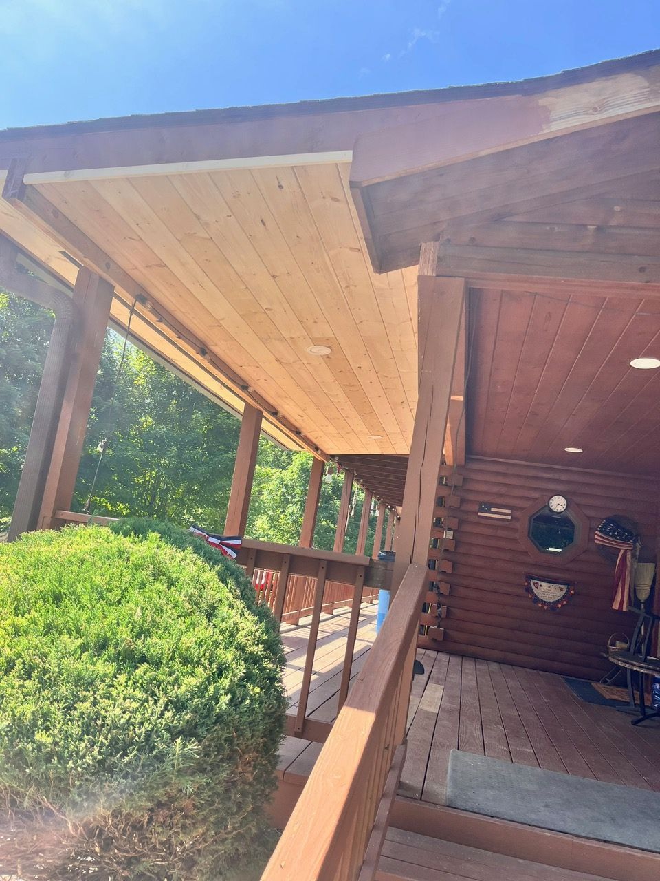 A wooden porch with a blue sky in the background and a bush in the foreground.
