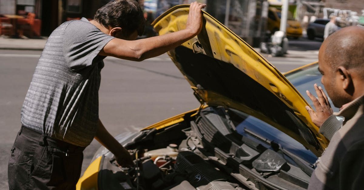 A man is looking under the hood of a yellow car.  | AutoWits