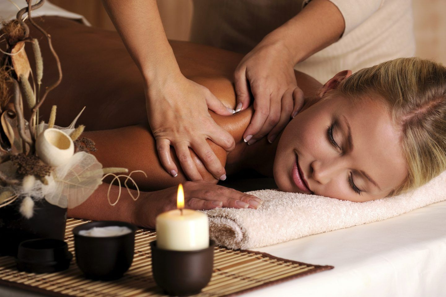 A Woman is Getting a Massage at a Spa With a Candle — Naked Skin Day Spa & Cocktail Lounge in Sunshine Coast, QLD