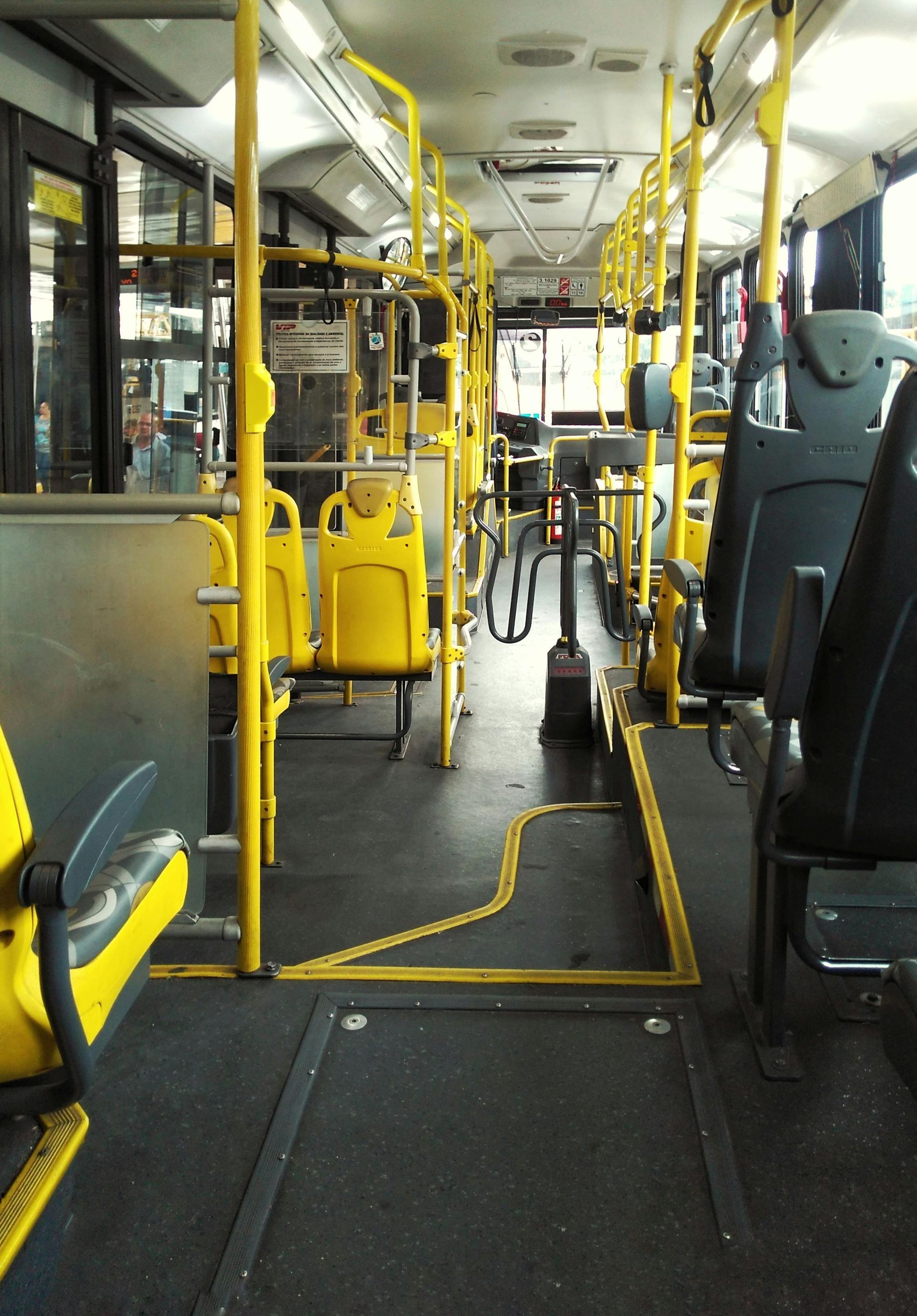 Interior of a yellow and gray bus. Black seats line the sides, yellow poles and railings throughout.