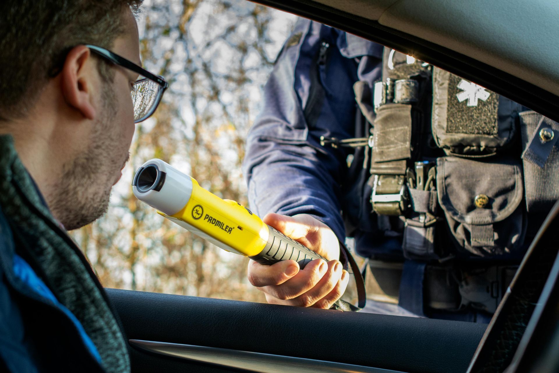 Man in car taking a breathalyzer test from a police officer.