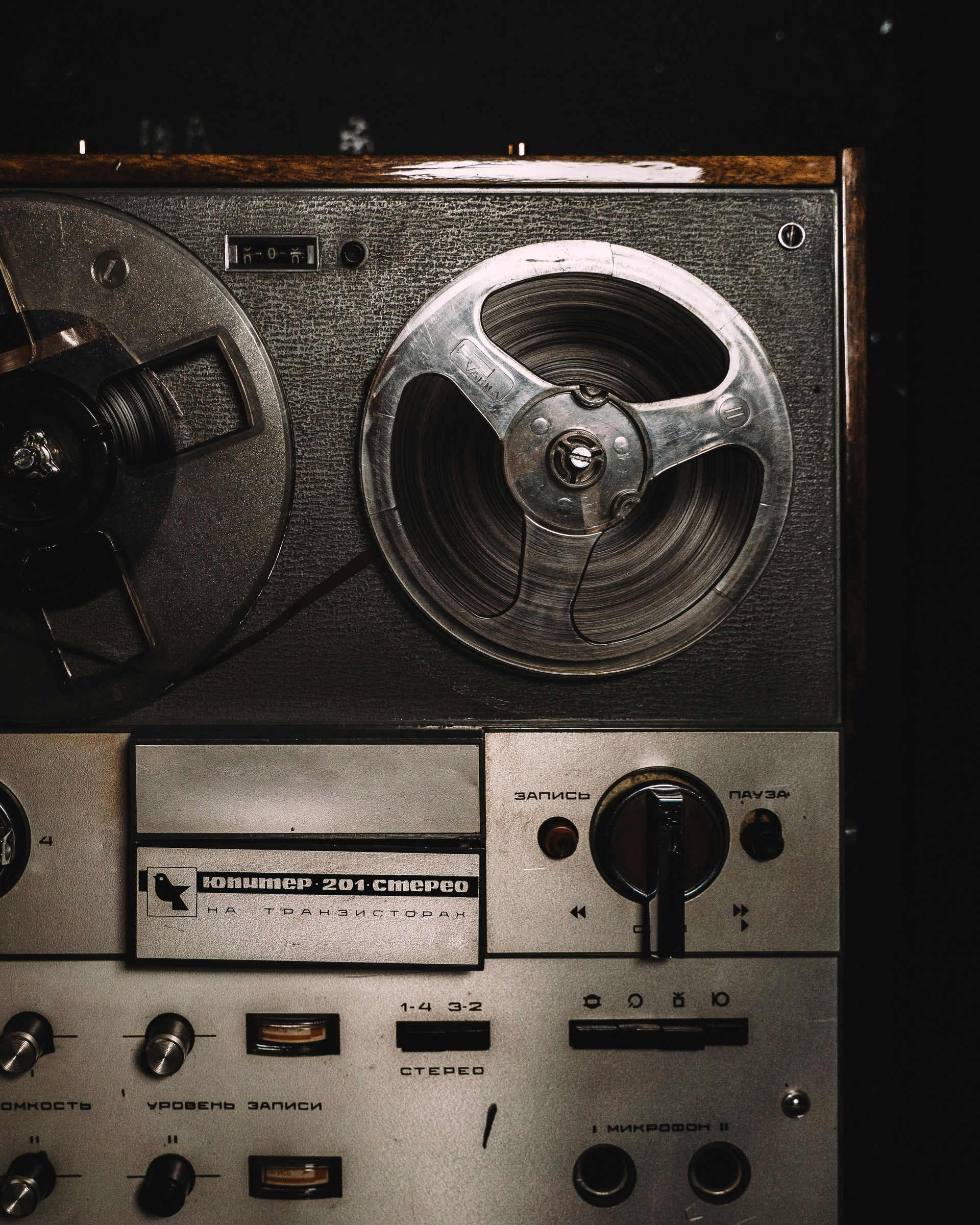 Vintage reel-to-reel tape recorder.  Silver and wood tones against a dark background.