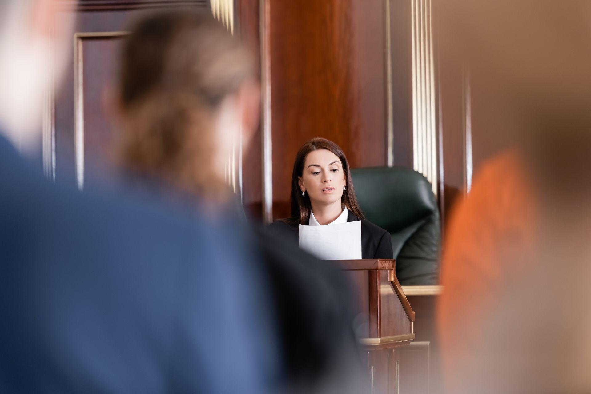 A judge reading from a document in court near people in a blurred foreground.