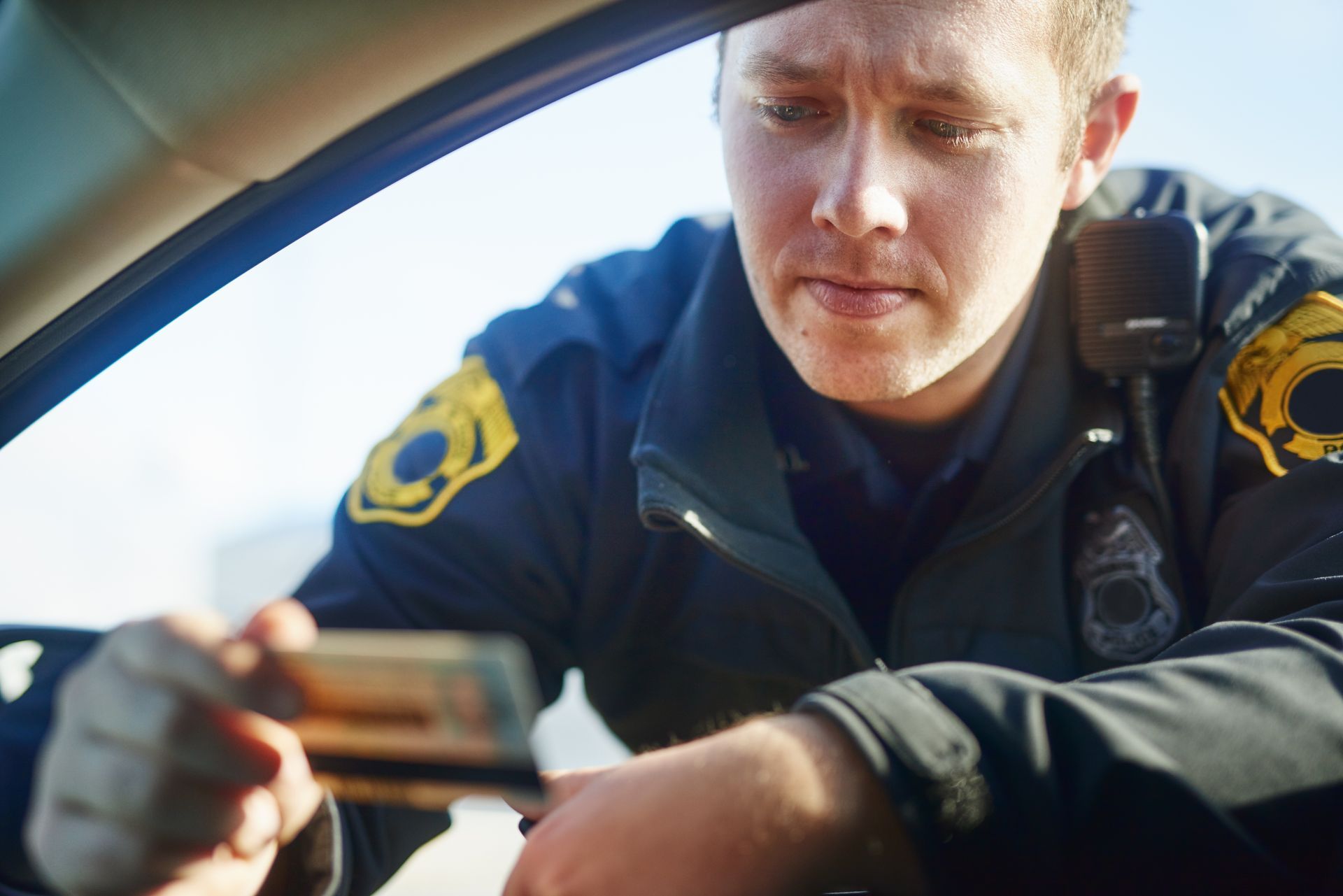 Police officer leaning toward a car window, looking down at something inside.