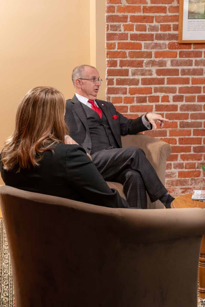 A man and a woman are sitting in chairs in front of a brick wall.