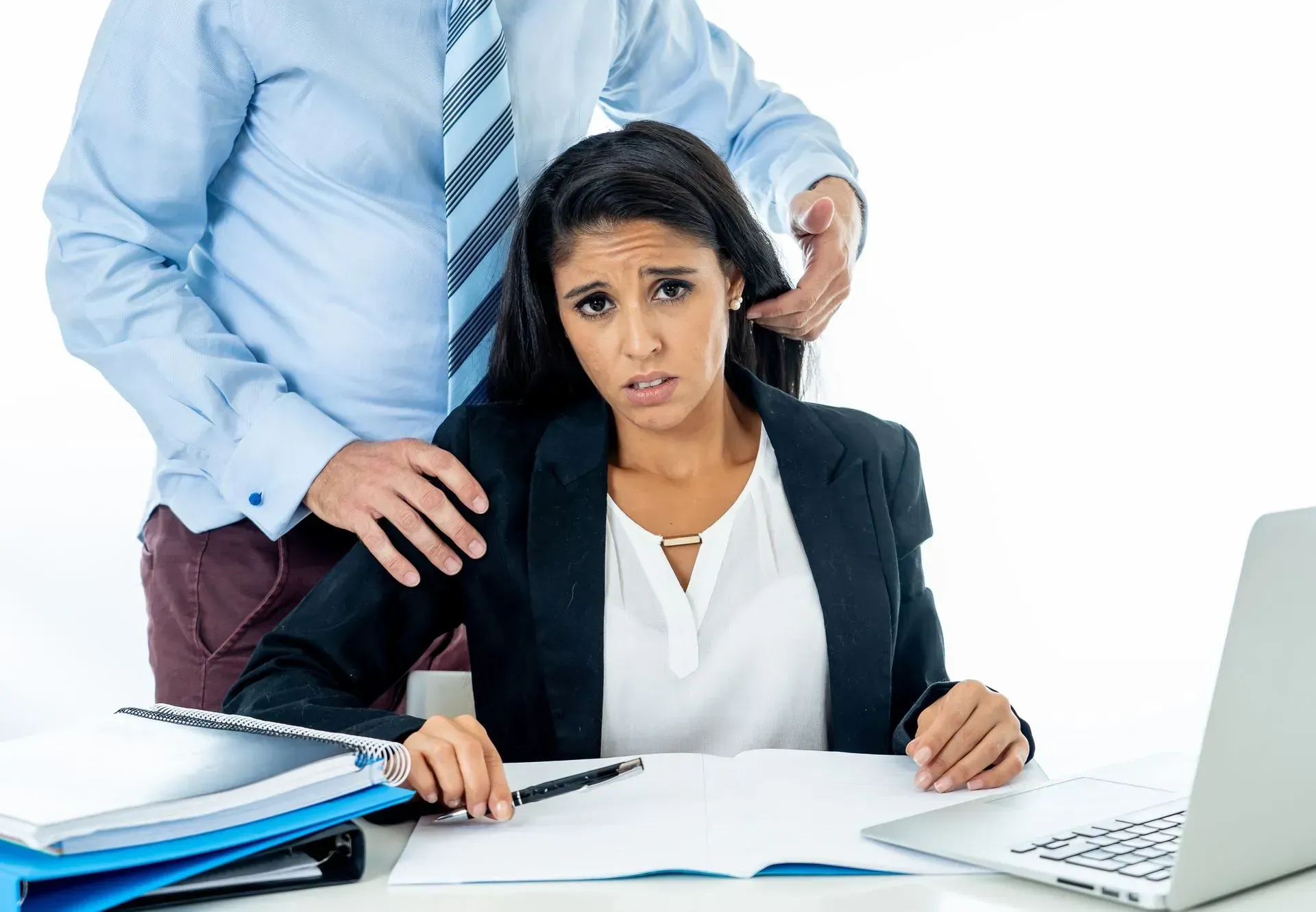 A woman is sitting at a desk with a laptop and a man is touching her shoulder.