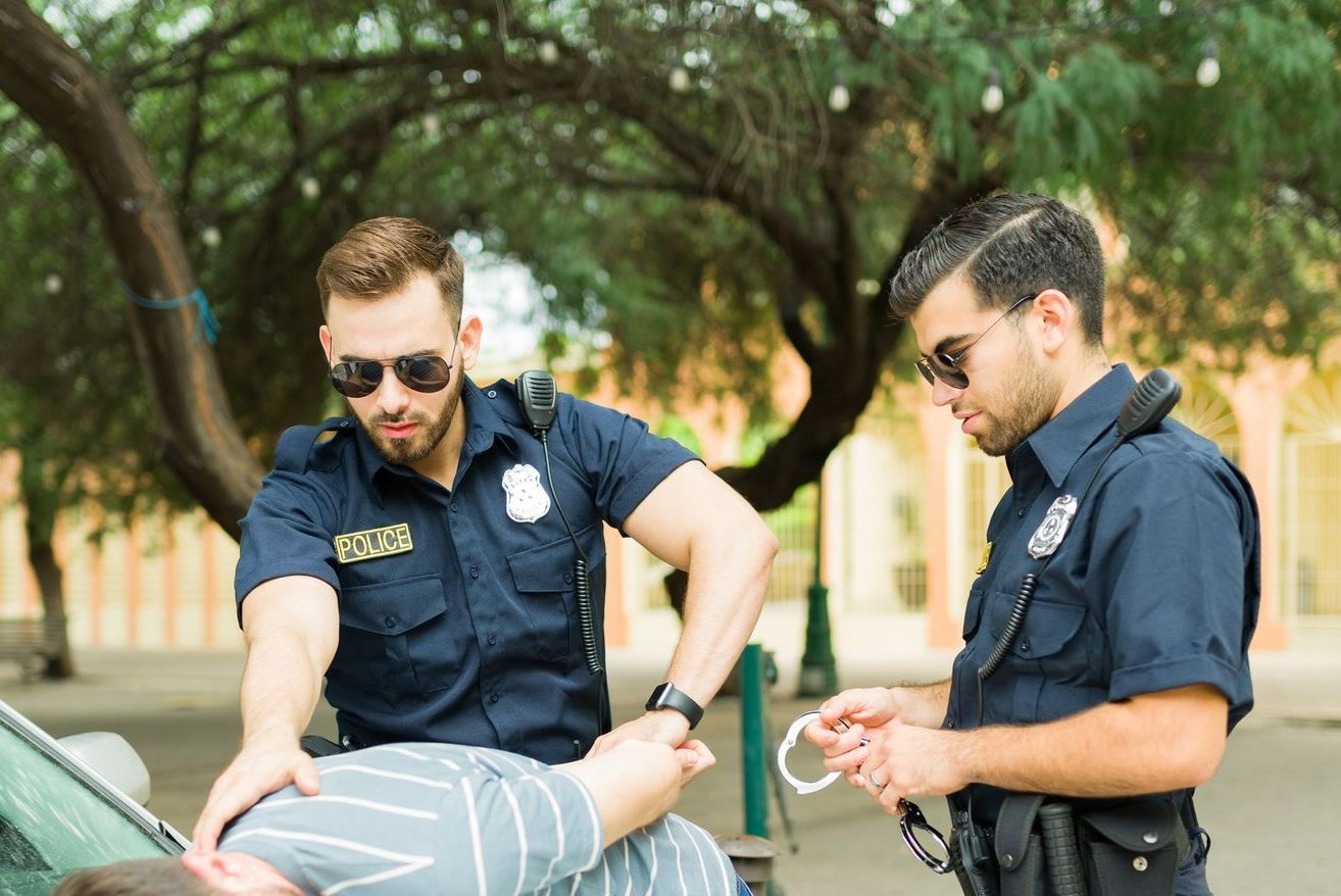 Two police officers are arresting a man in a parking lot.