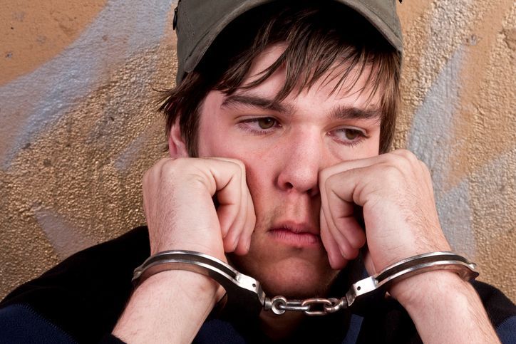 A young man is wearing handcuffs and a hat.