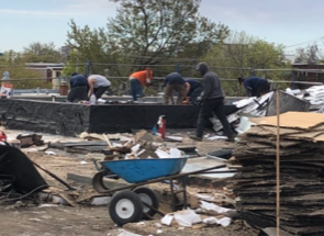 Un groupe d'hommes travaille sur un toit avec une brouette au premier plan