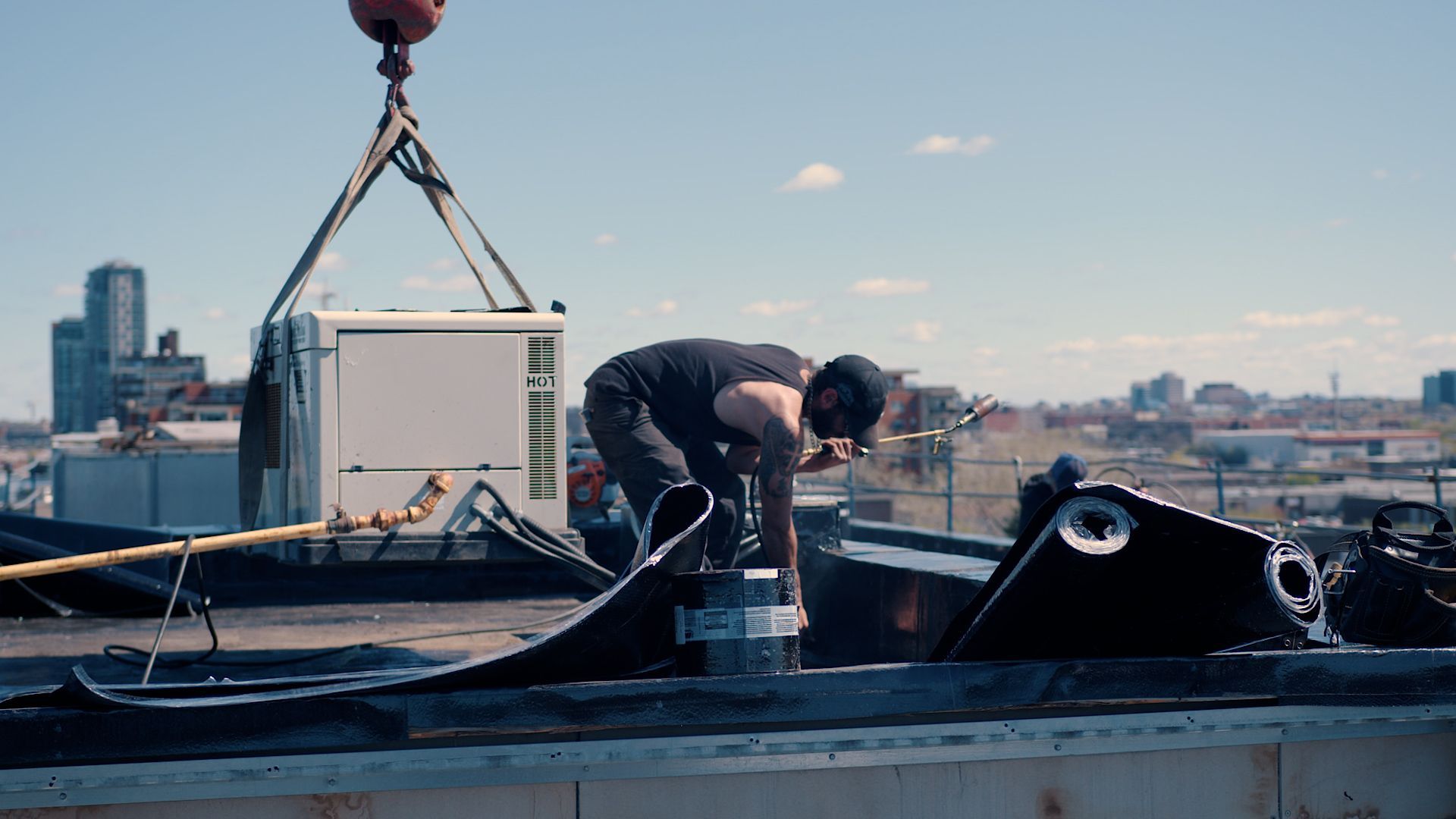 Un homme travaille sur un toit avec une grue en arrière-plan.