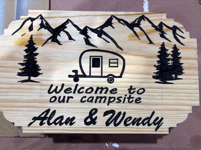 Wooden campsite sign with mountains, camper, trees, and 
