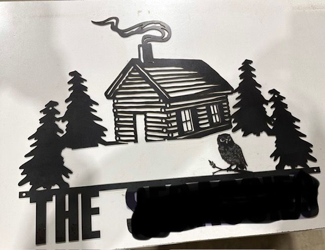 Black metal sign of cabin, trees, owl, and 