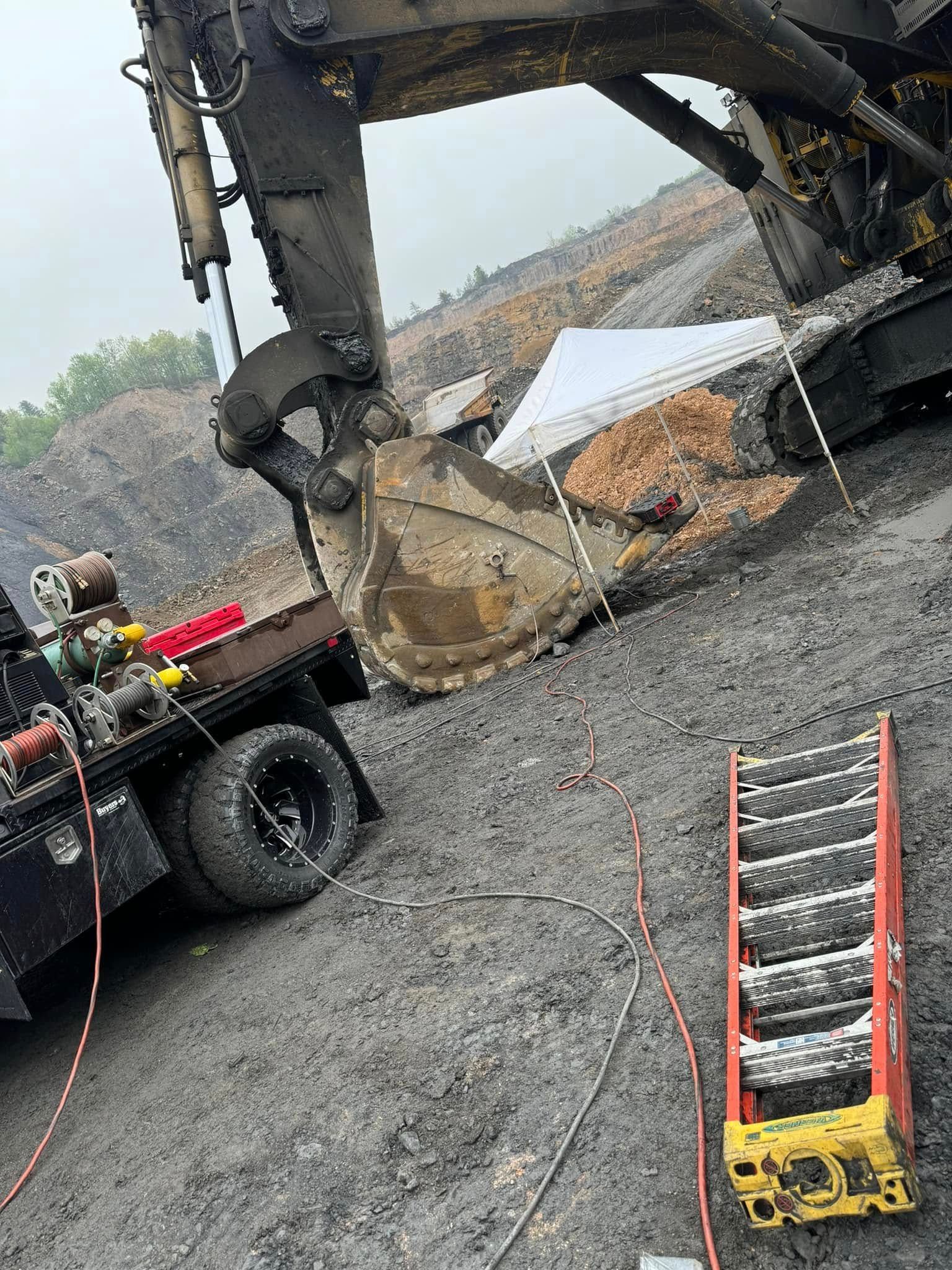 A large excavator next to a truck, on a dark, muddy surface, with a ladder.