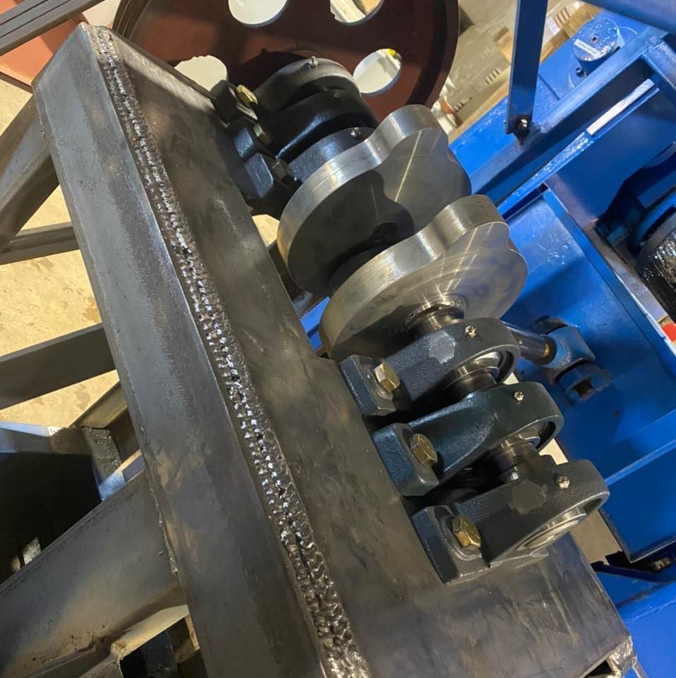 A metal crankshaft mounted on a blue machine frame, welded metal supports, close up.