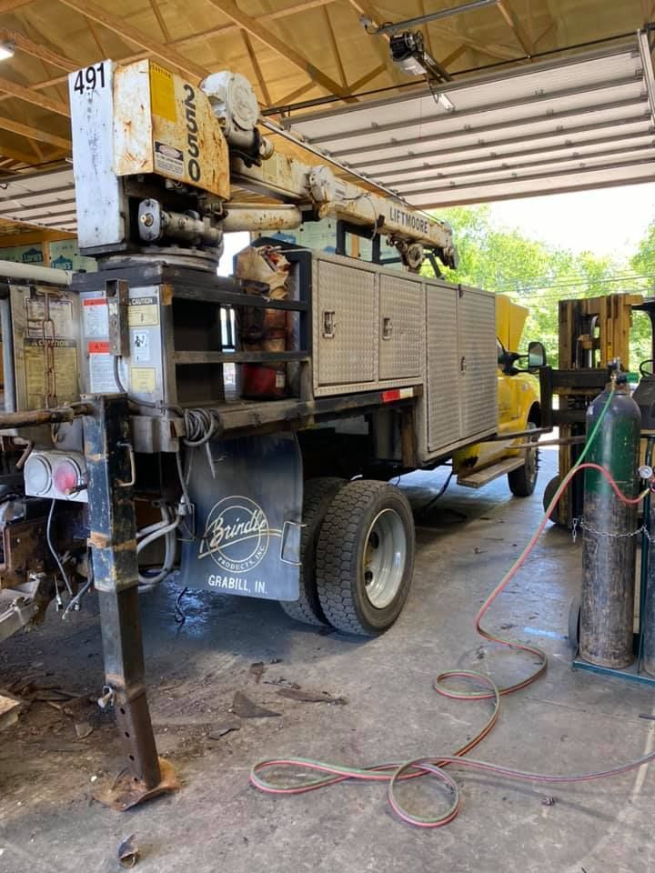 A utility truck is parked in a garage next to a forklift.