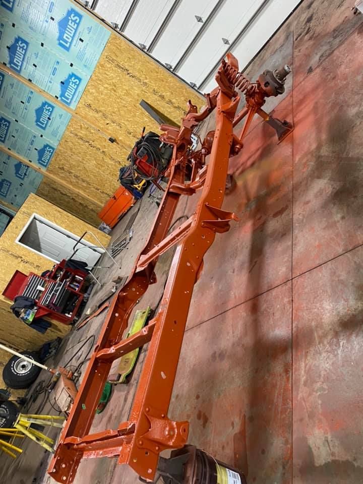 Orange painted vehicle frame in a garage, with other parts and equipment visible.