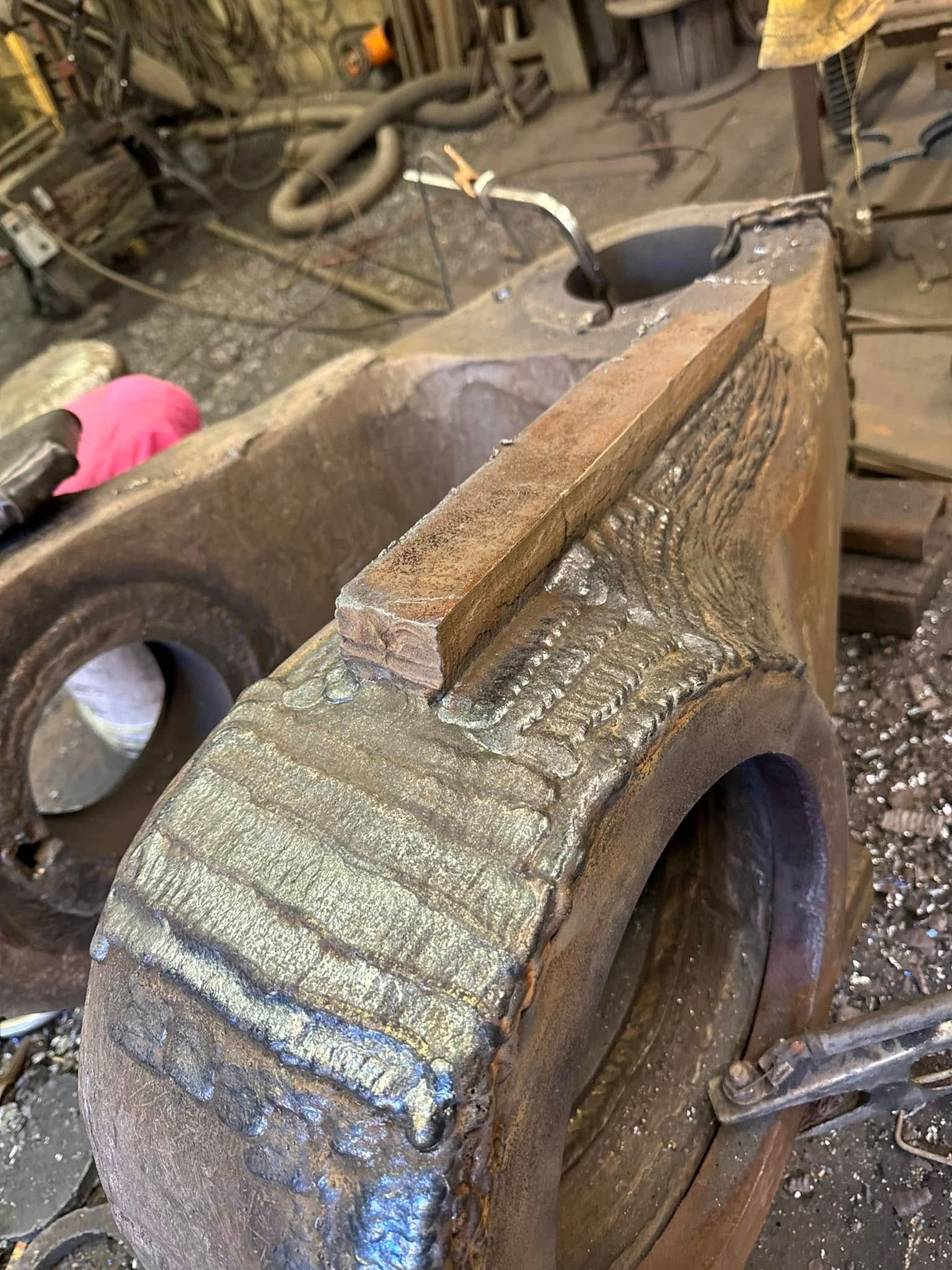 Large, industrial metal part with welded bar, inside a workshop.