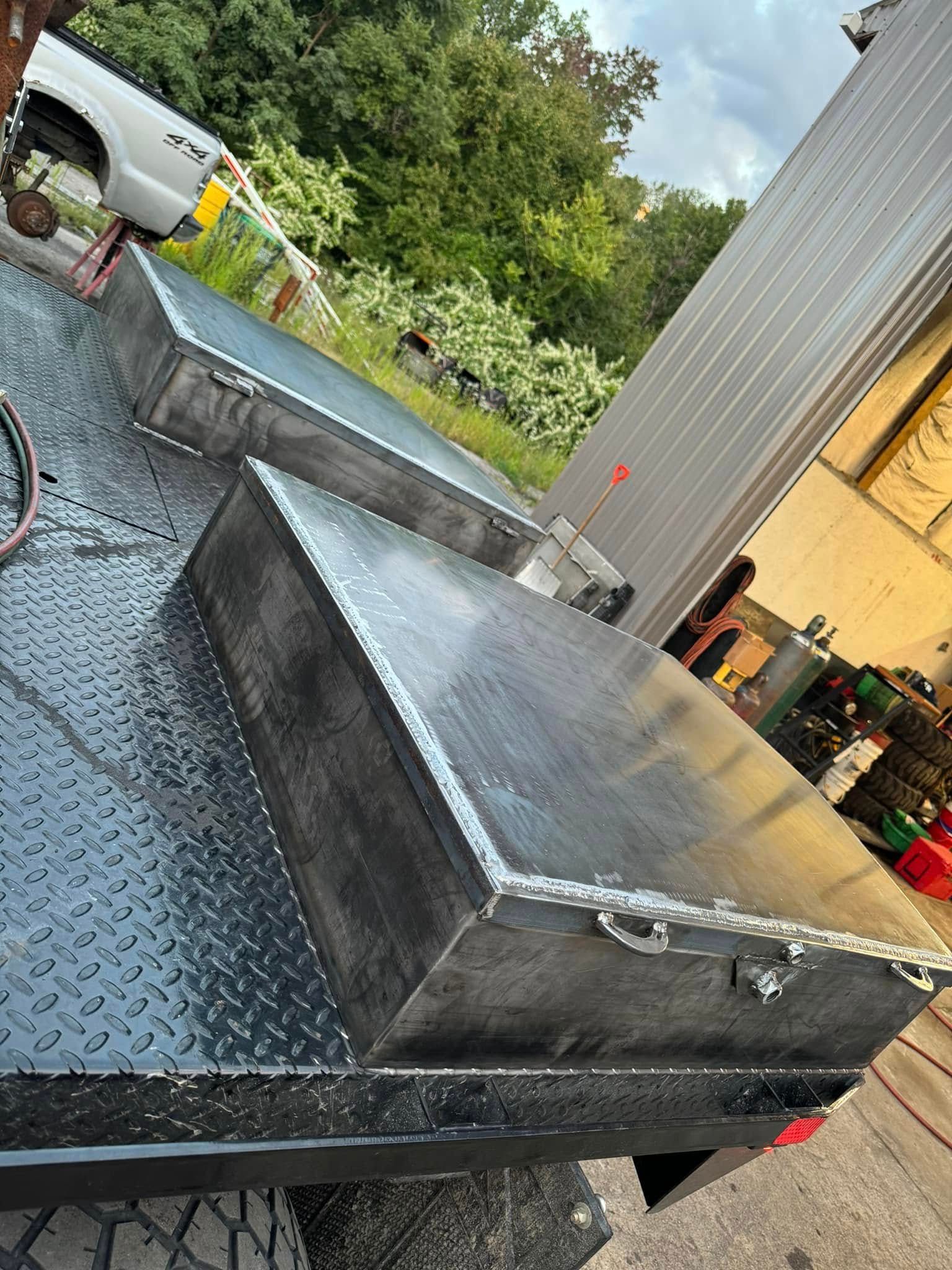 A black flatbed truck with two metal storage boxes, in an outdoor setting.