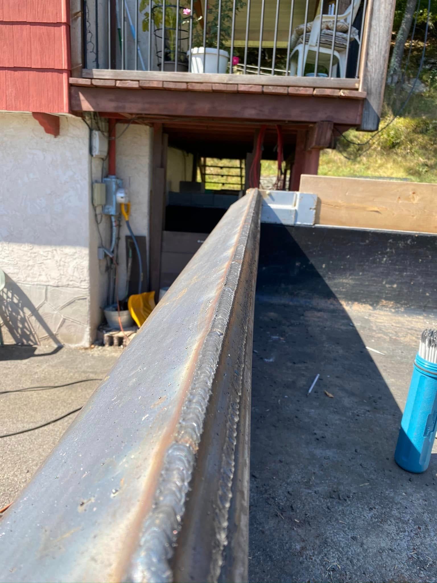 Welded metal beam in front of a deck and concrete surface, with welding tools to the right.