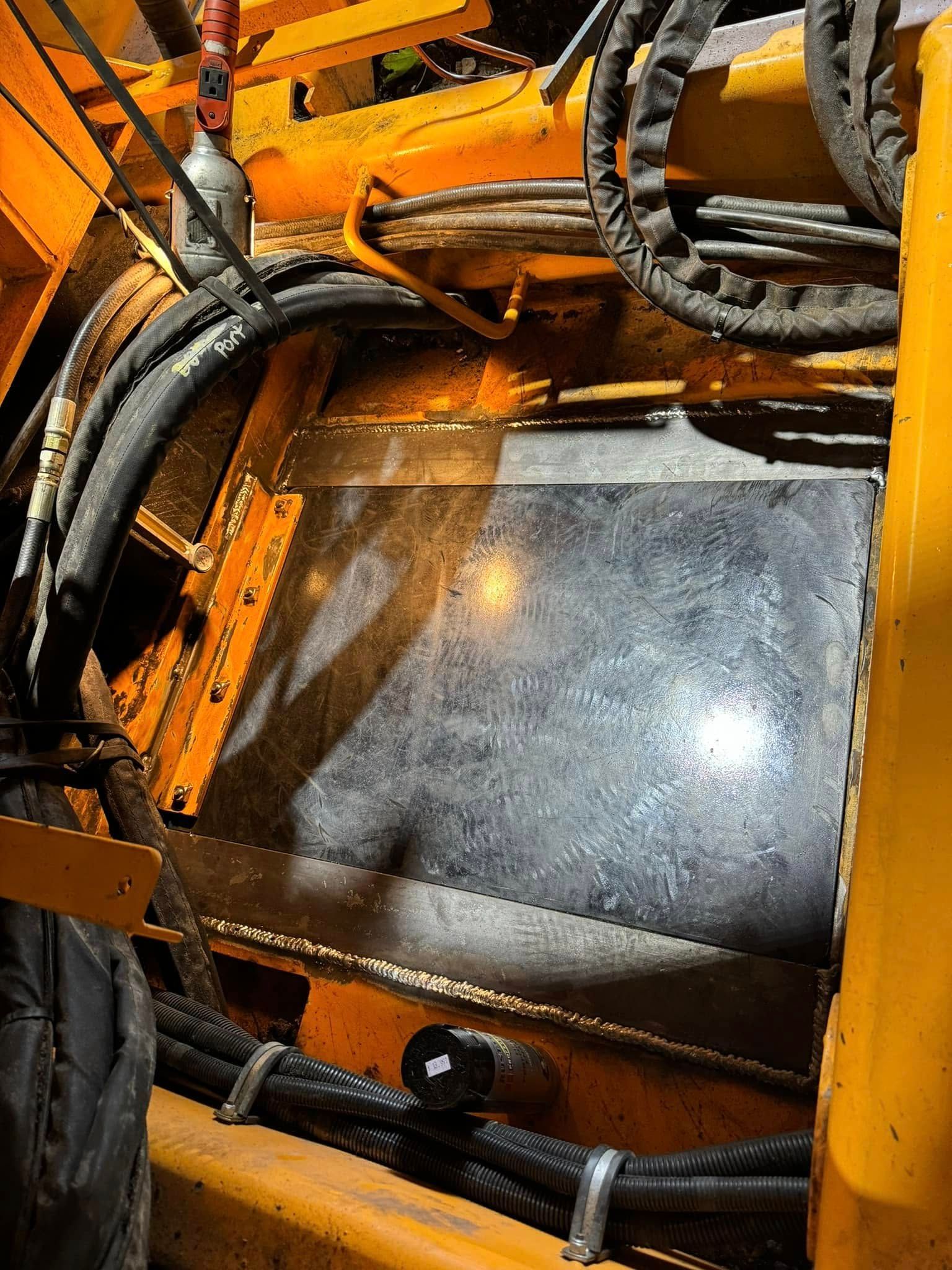 Close-up of yellow industrial machine with dark hoses and a metal panel.