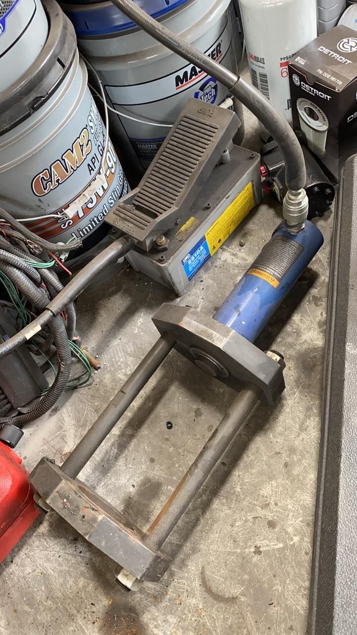 Hydraulic press with blue cylinder, foot pedal, and metal frame on a workbench.