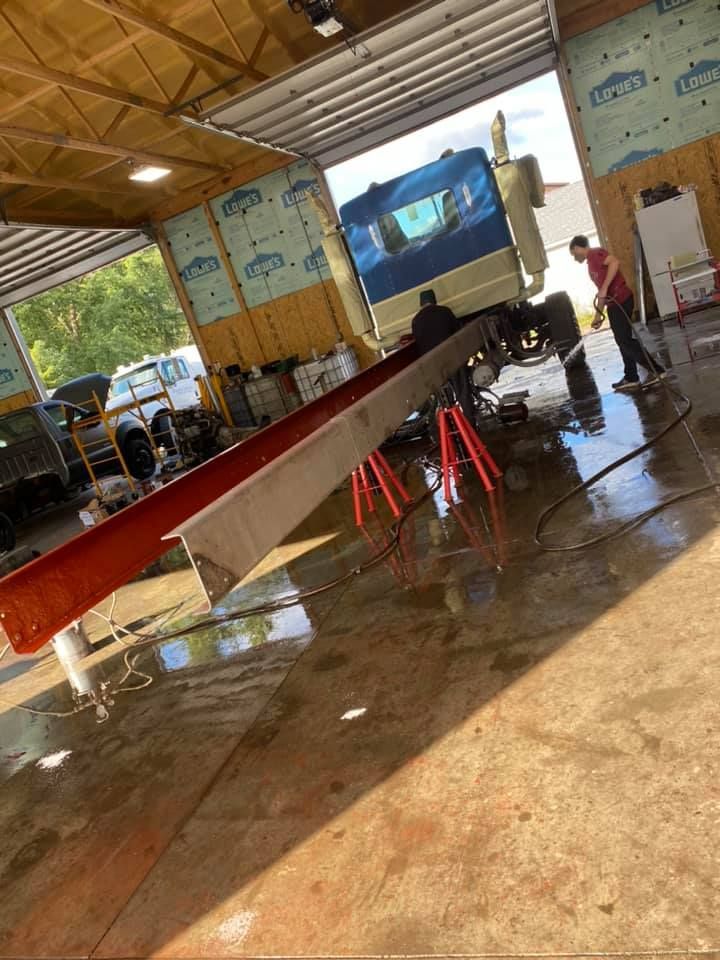 Workers repairing a truck in a garage; a long metal beam is supported by red jack stands.
