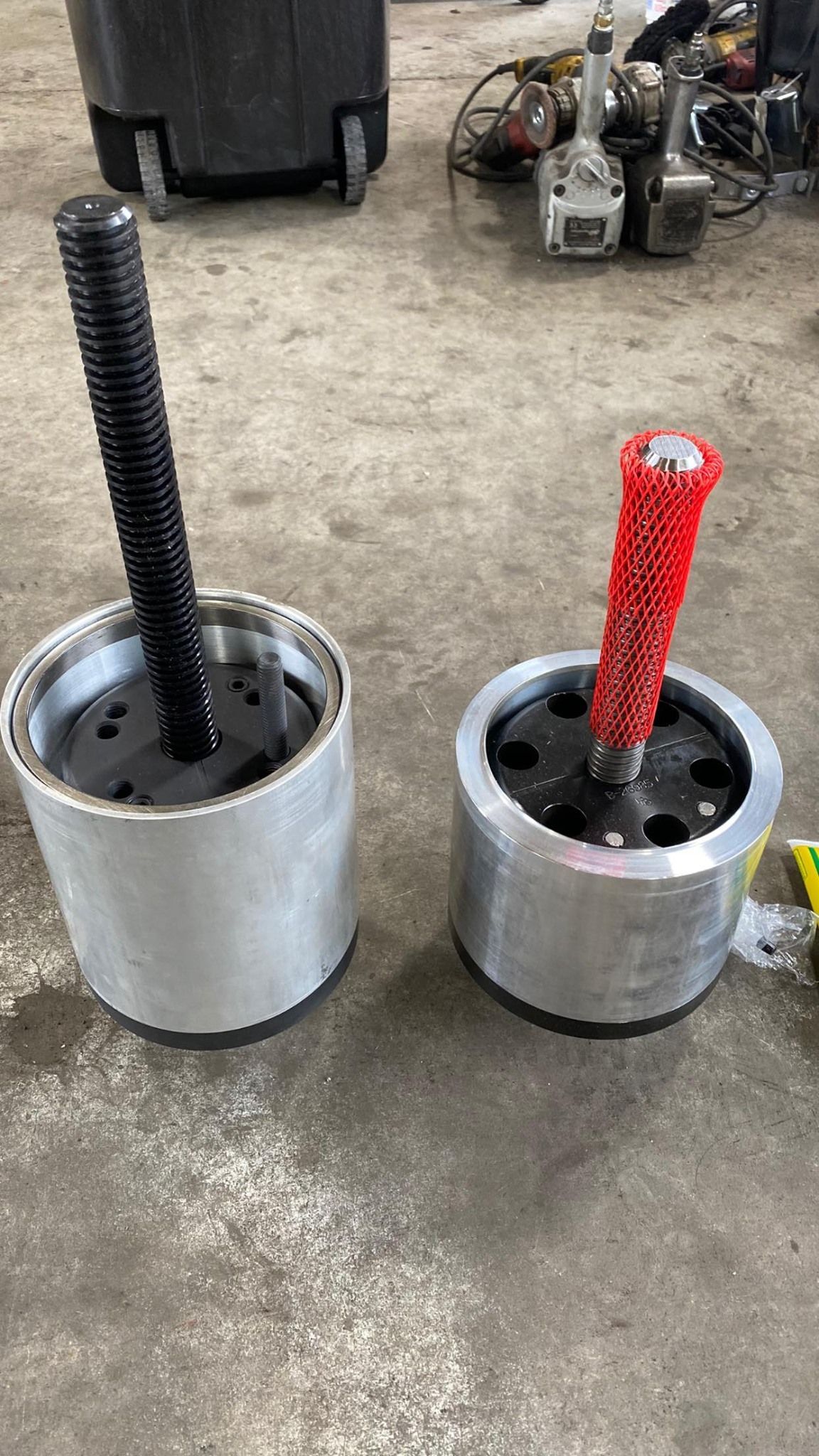 Two cylindrical tools with threaded shafts, one black, one red, on a concrete surface.