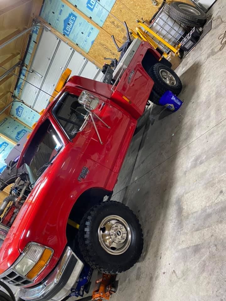 Red Ford pickup truck in a garage setting, wheels off the ground, tools visible.