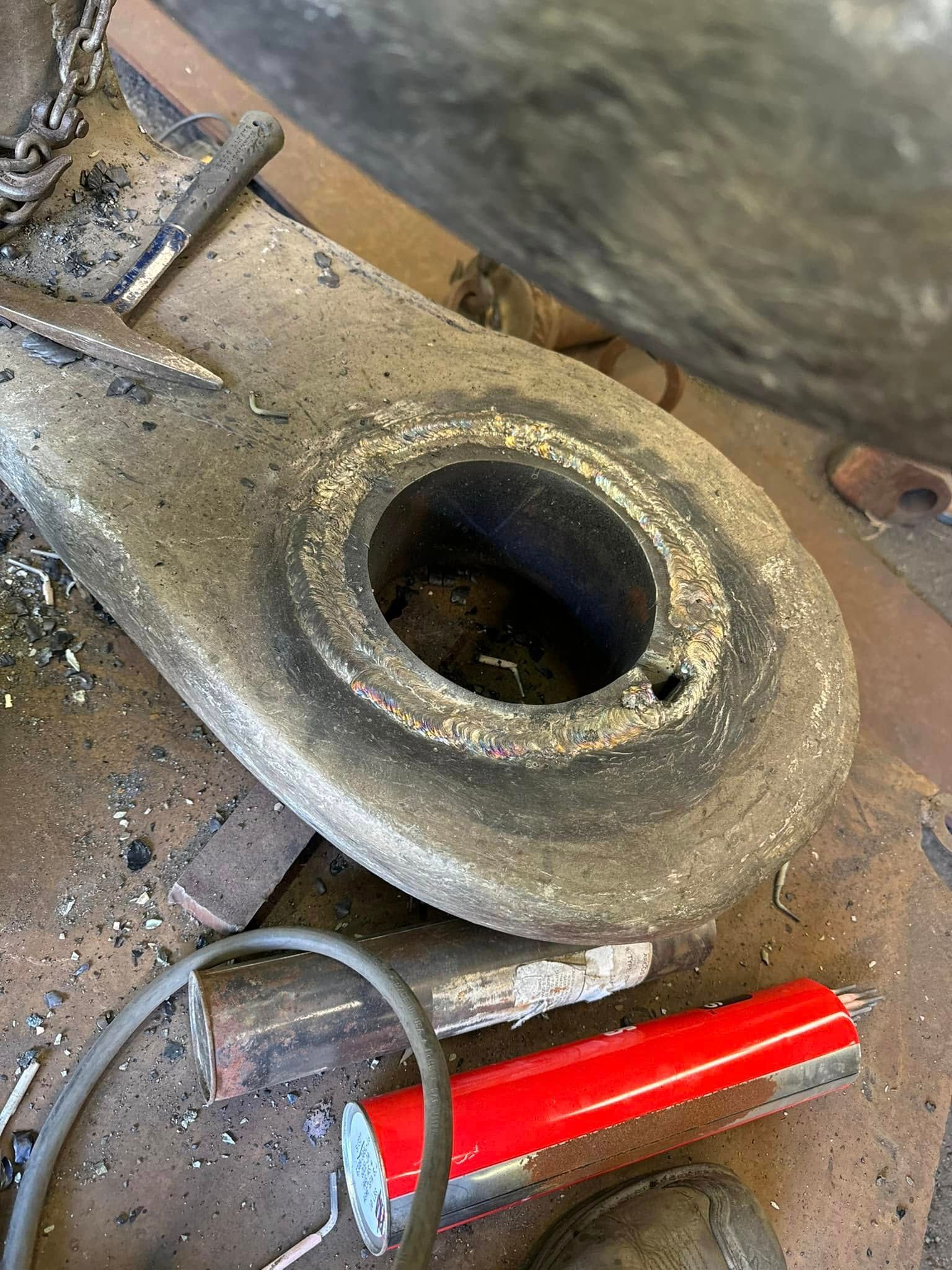 Large, grey metal eyelet with a central hole, lying on a workbench. Red object in the foreground.