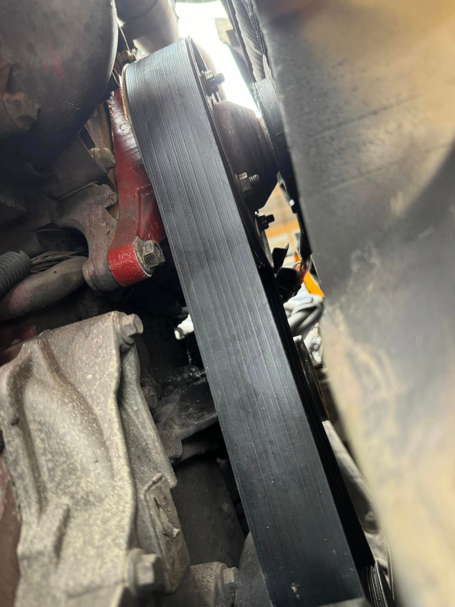 Black belt on a car engine, partially obscured by metal and components.