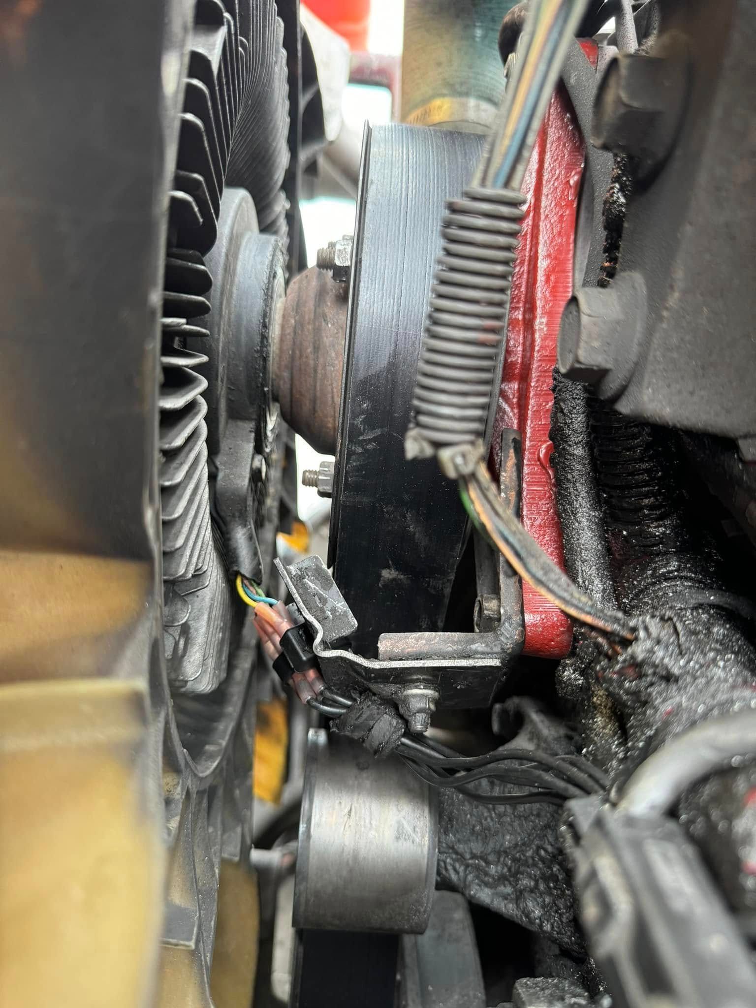 Engine fan and belt assembly with wires, covered in black fluid.