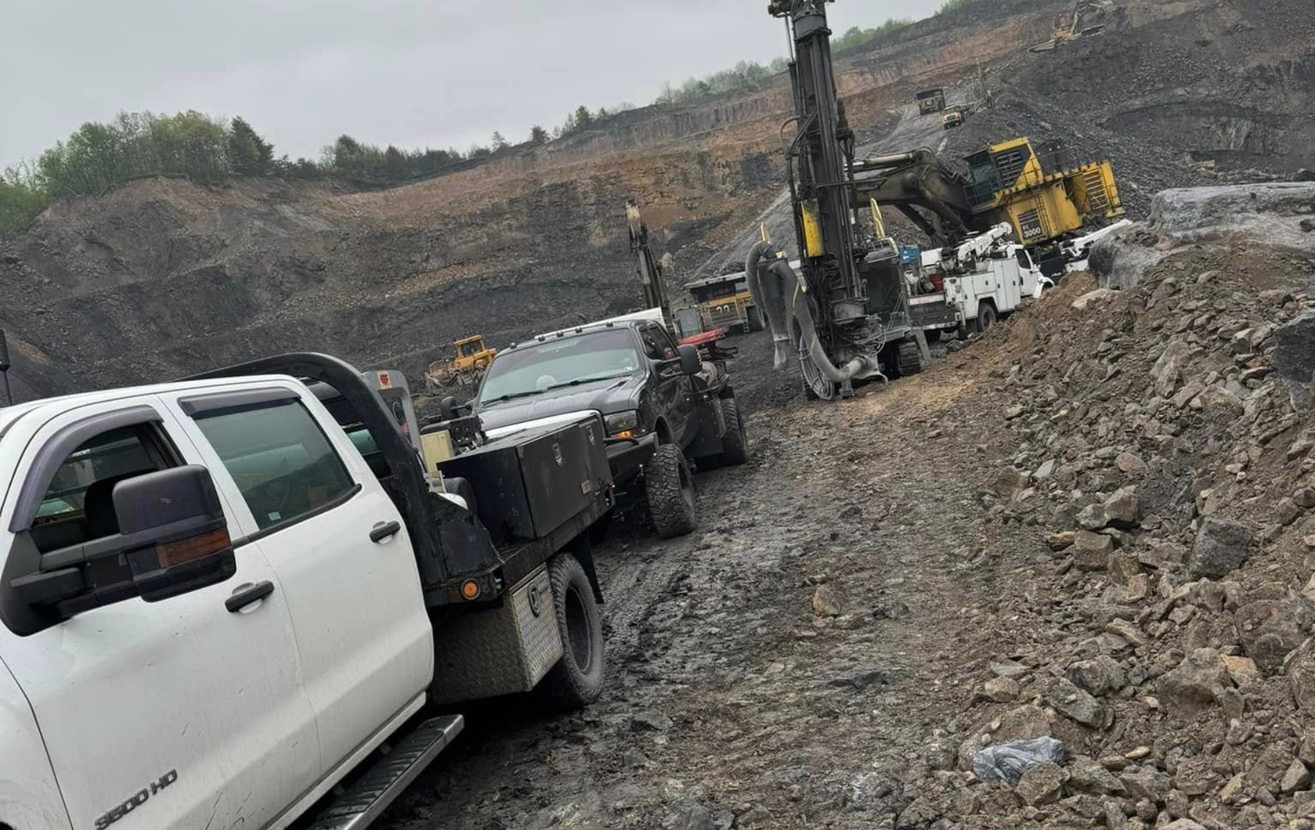 A white truck is towing a dump truck in a rocky area.