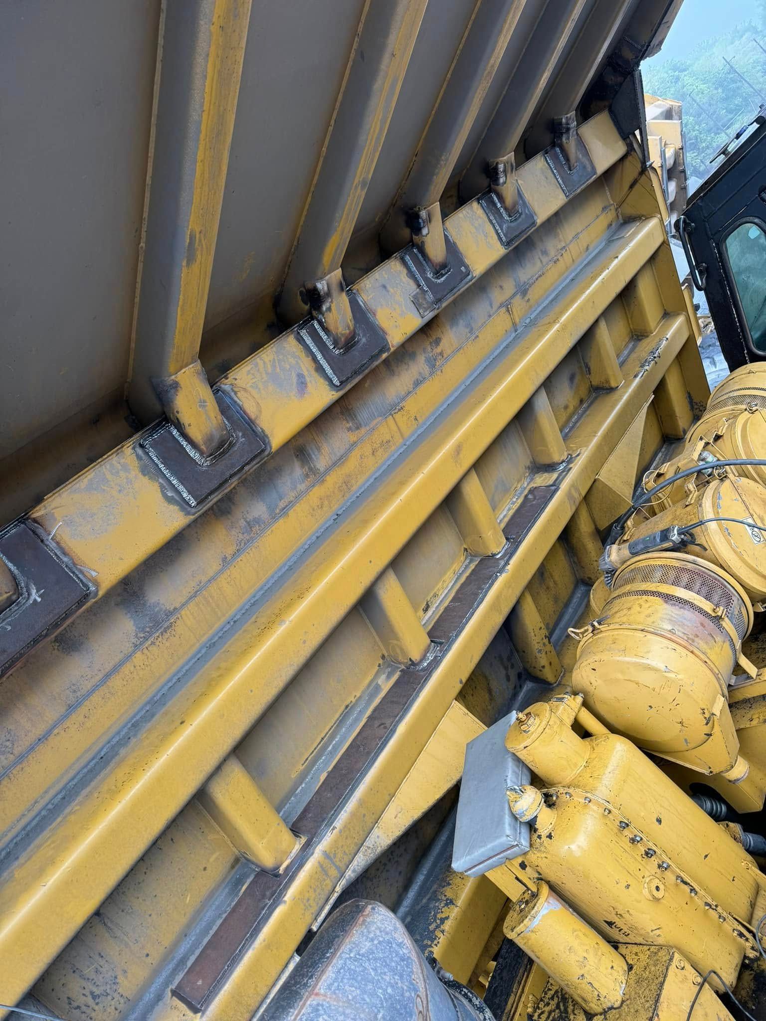 Yellow heavy machinery components; a side view of a blade and supports, with welded construction details.